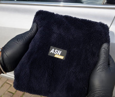 Zachte zwarte ASN microvezeldoek in twee handen naast een auto