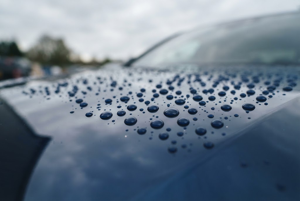 Waterdruppels parelen af op de gecoate motorkap van een donkerblauwe auto
