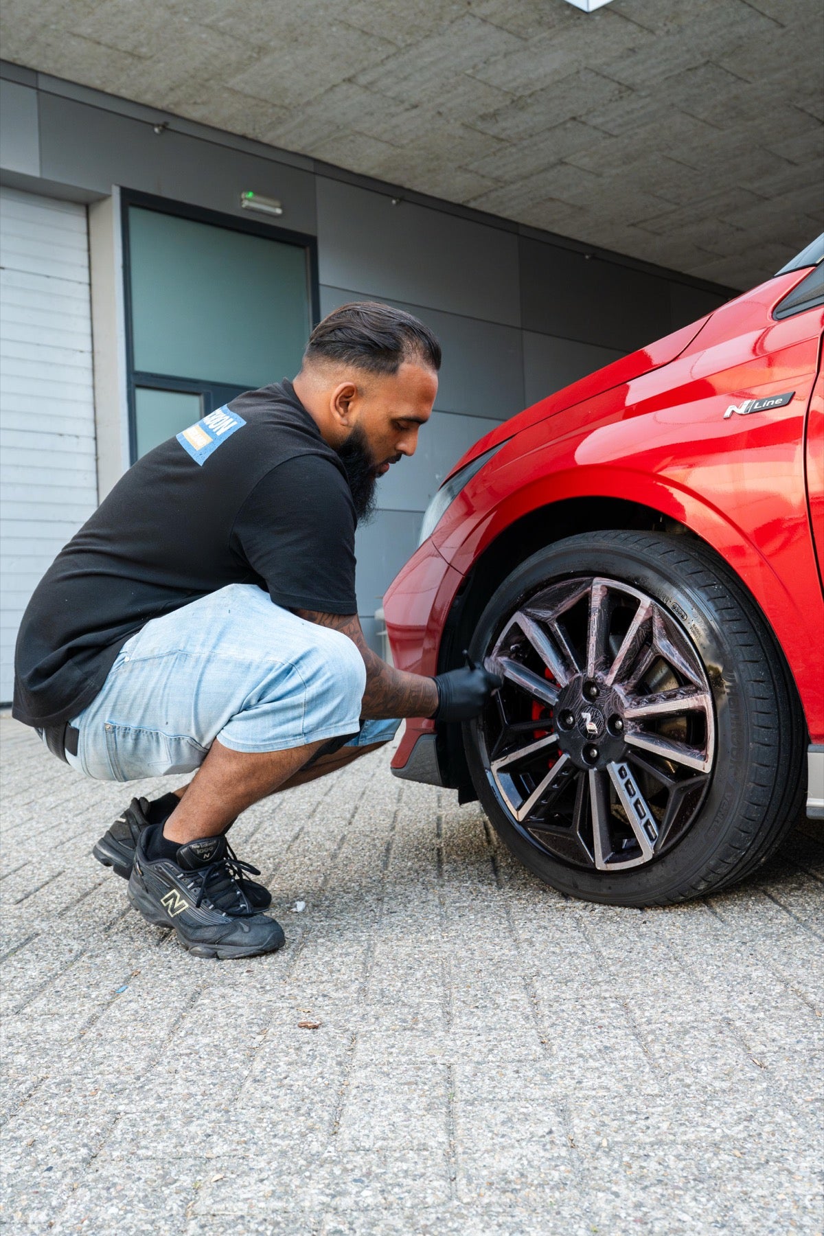 Medewerker van Auto Schoon Nederland reinigt de velg van een rode auto