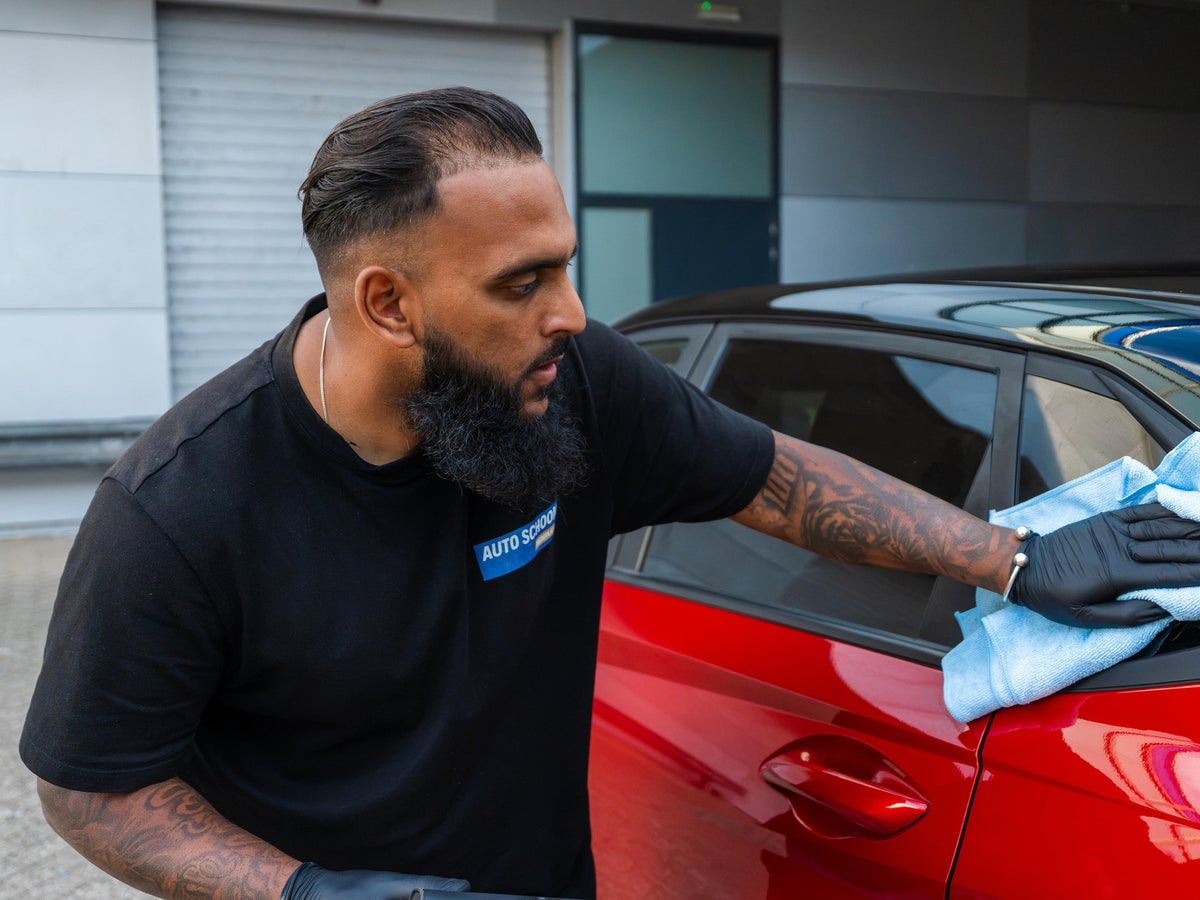 Medewerker poetst de motorkap van een rode auto na met een microvezeldoek