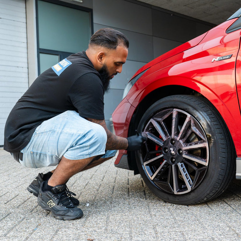 Medewerker reinigt de velg van een rode auto